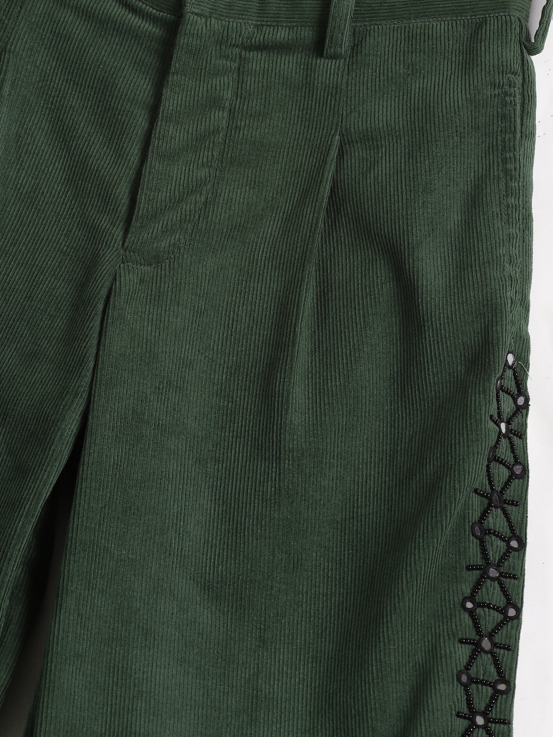 Green corduroy pants with a button and lace-up detail on a white background