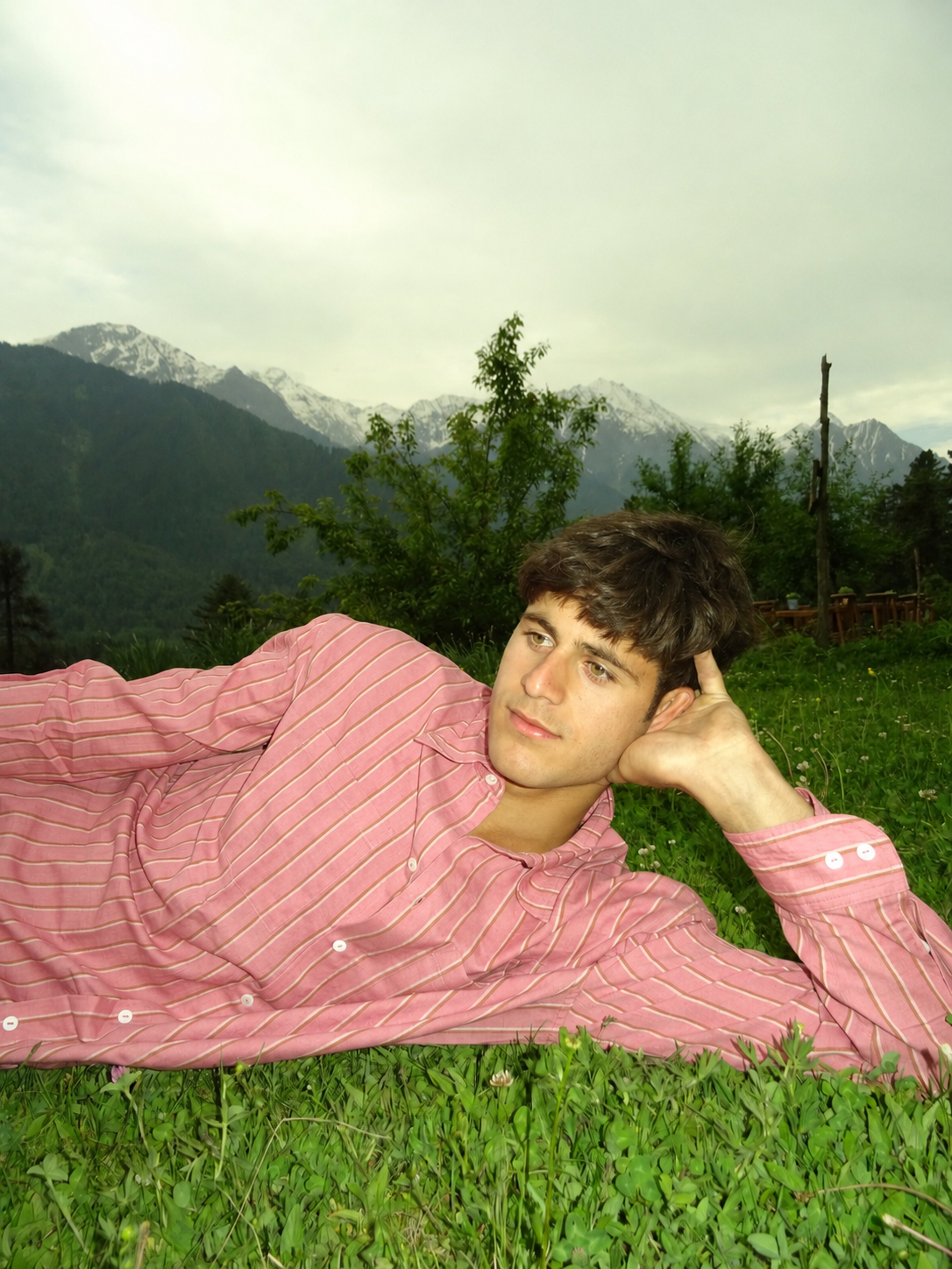 Person in a pink shirt lying on grass with mountains in the background