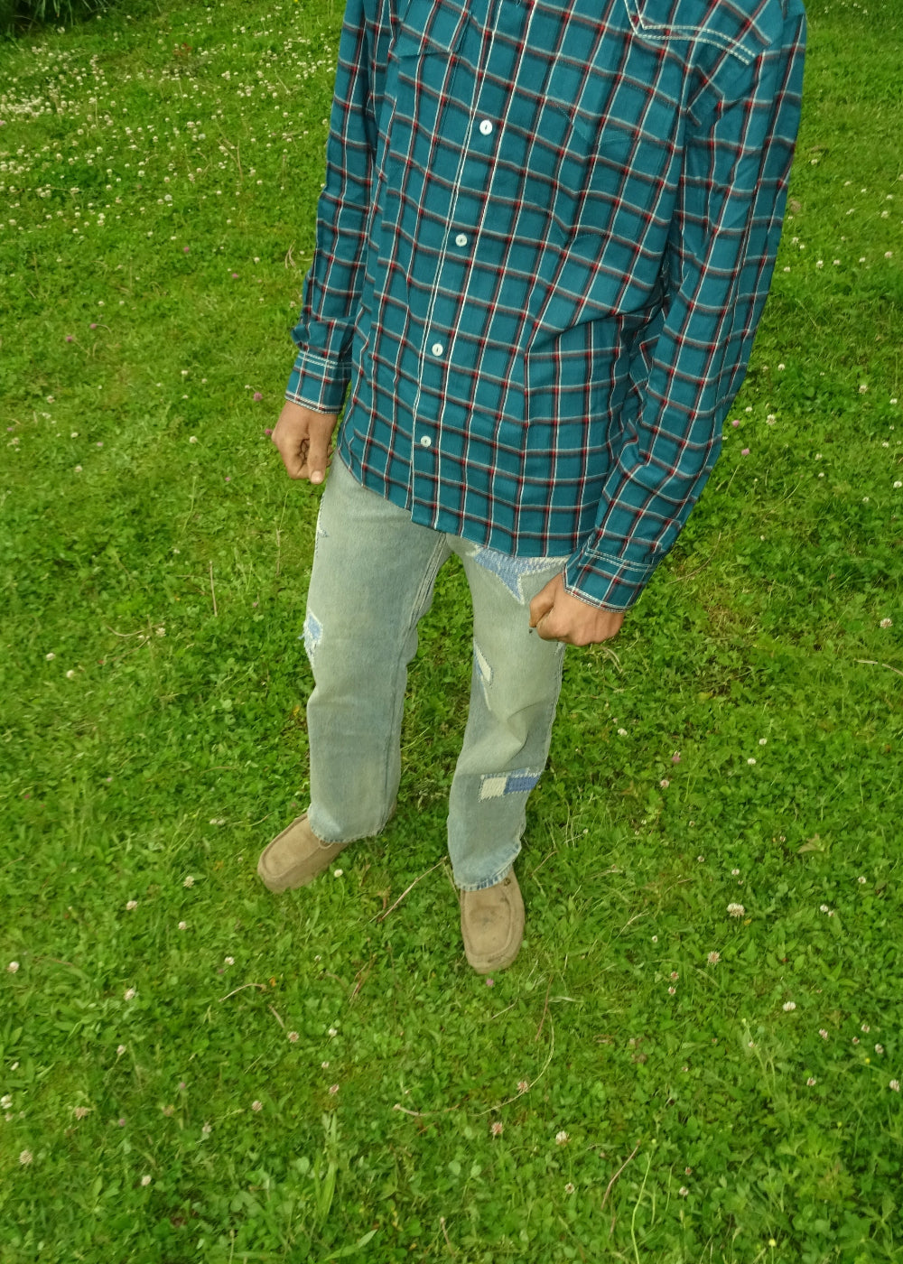 Person wearing a blue plaid shirt and light jeans standing on grass