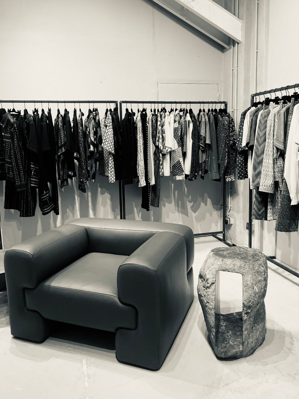 Black leather armchair and gray stool in front of clothing racks.