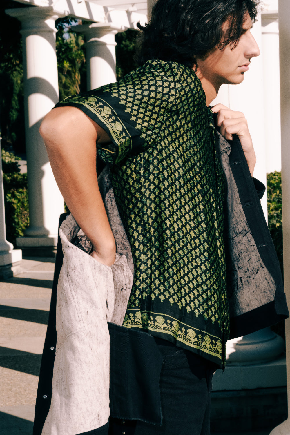 Person wearing a patterned green and black outfit with a white building in the background