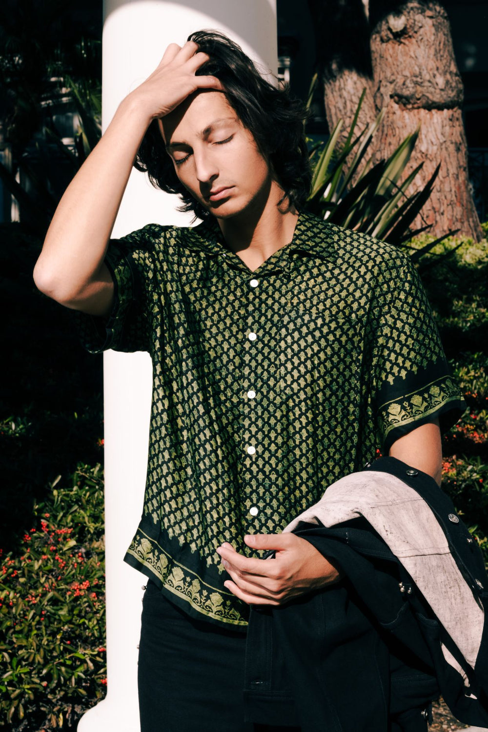 Person wearing a green patterned shirt outdoors with plants in the background