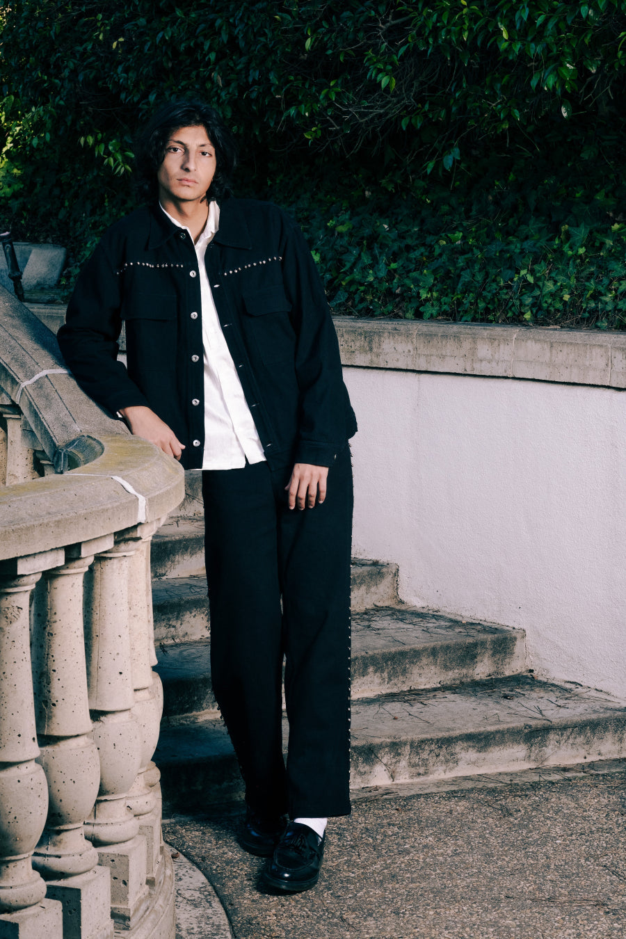 Person wearing a black jacket with text, standing on stone steps outdoors.