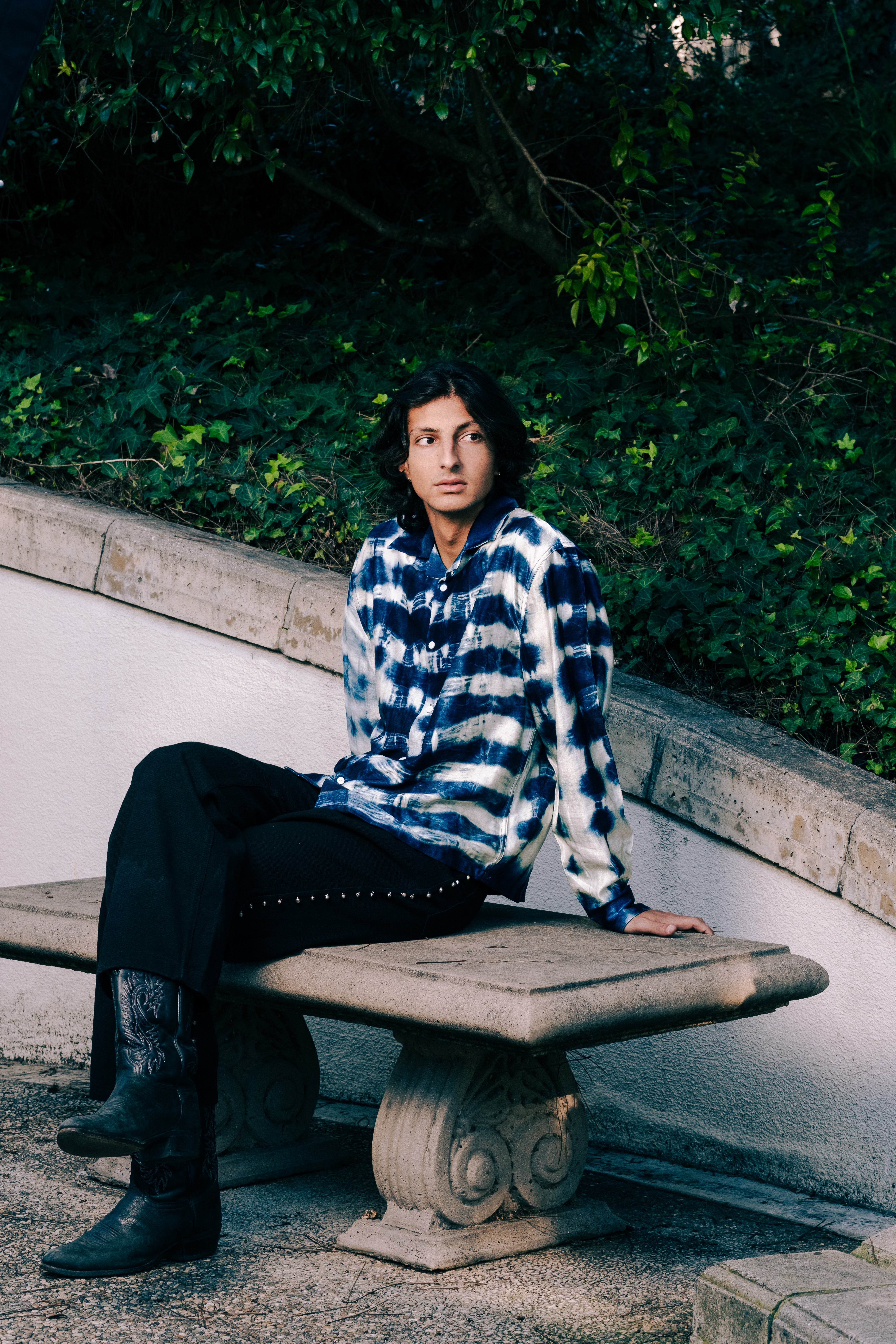 Person sitting on a stone bench with greenery in the background