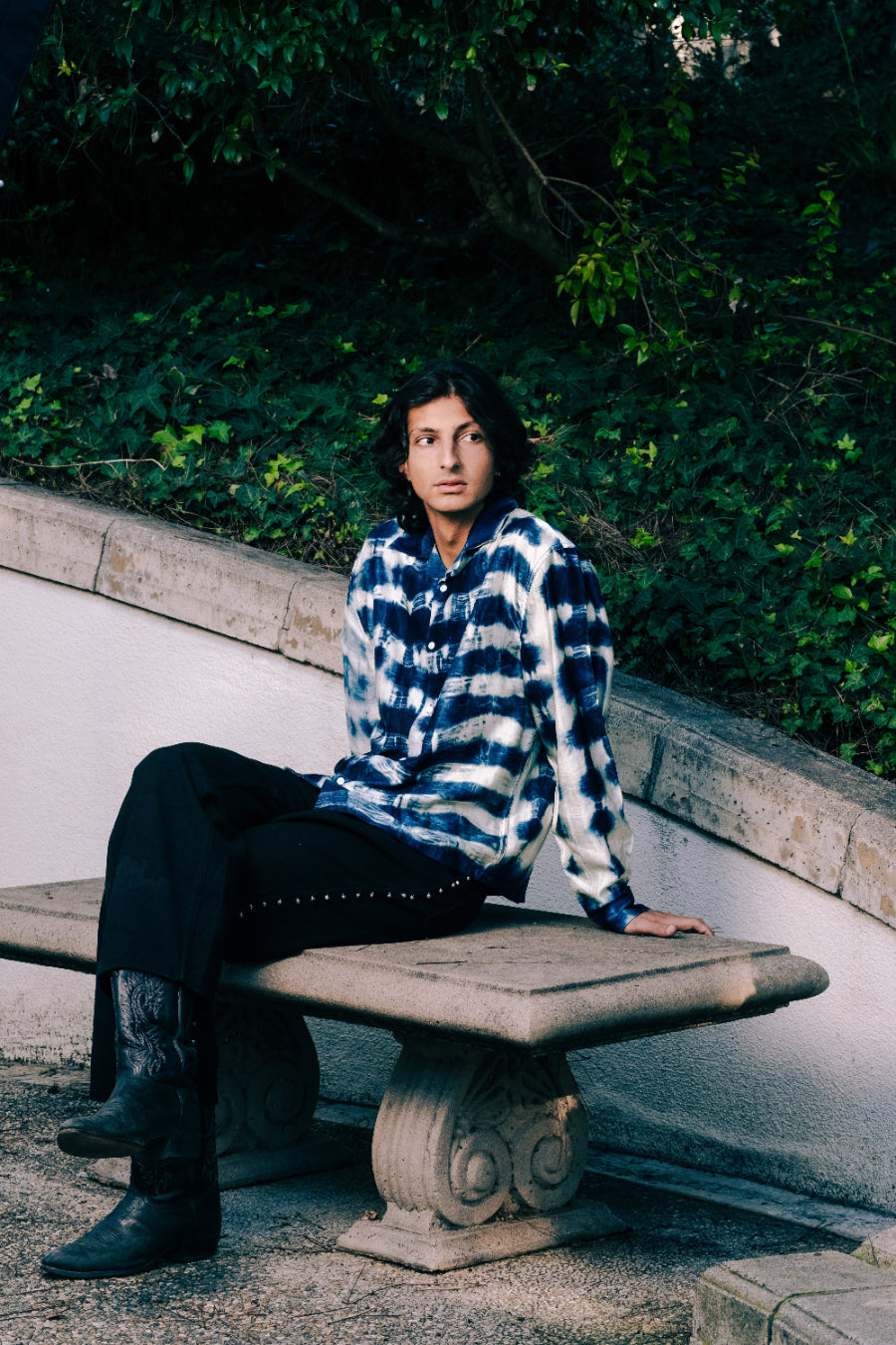 Person sitting on a stone bench with greenery in the background