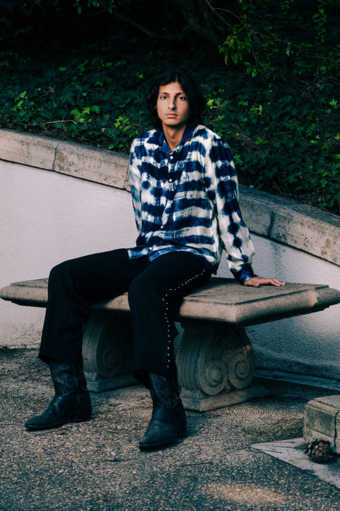 Person wearing a blue and white patterned shirt sitting on a stone bench outdoors.