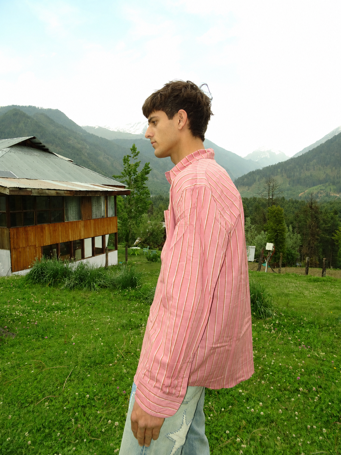 Person wearing a pink shirt standing in a grassy area with mountains in the background