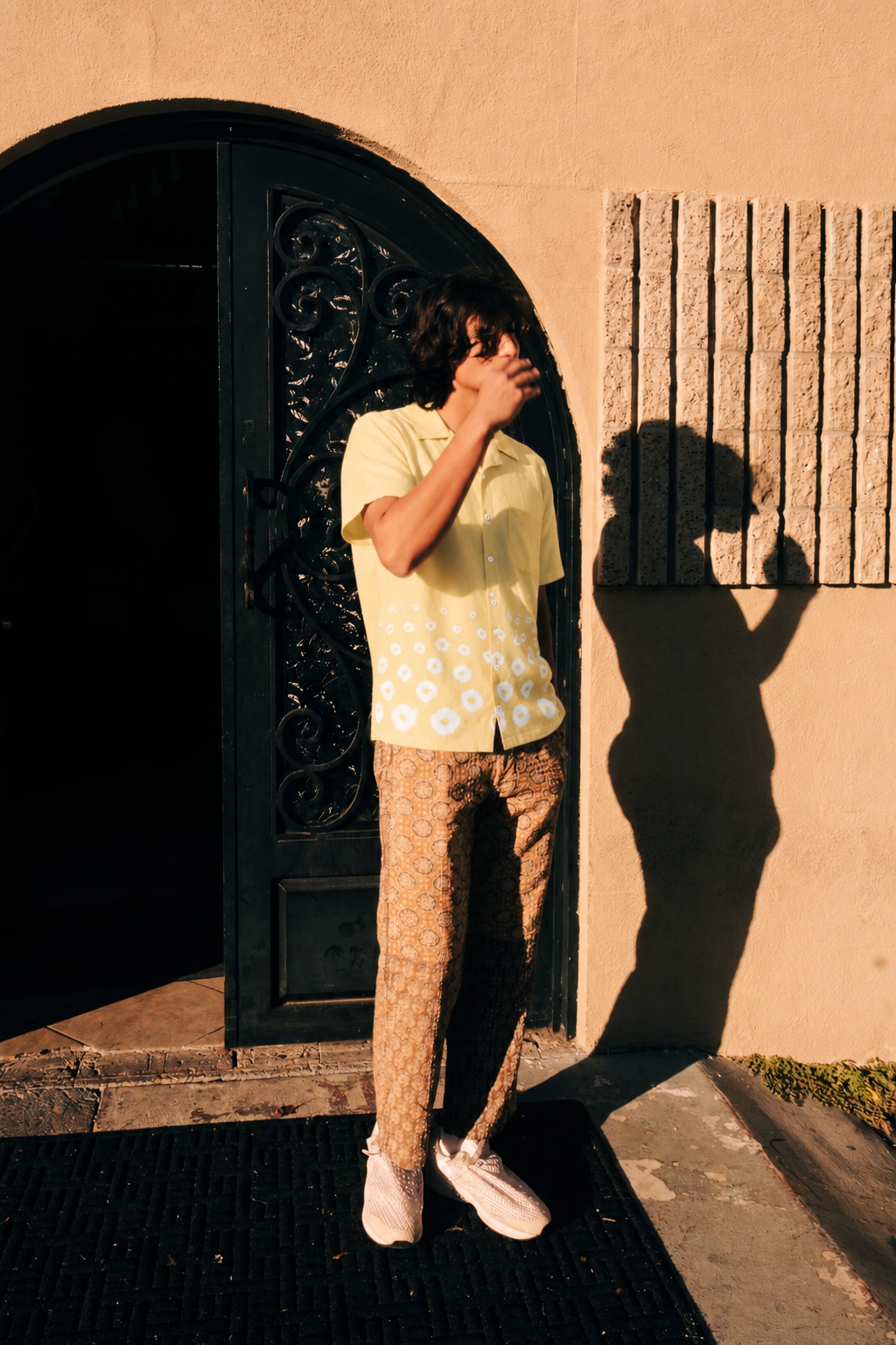 Person wearing a yellow bandhani-print shirt and printed trousers by a sunlit arched doorway – Hindostan Archive